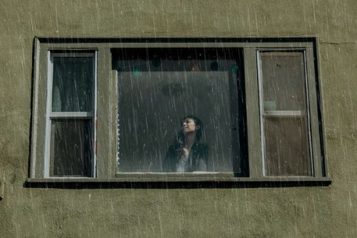 Woman looking out an open window during heavy rain on a home exterior